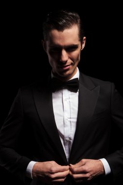 smiling elegant man posing in dark studio closing his jacket 