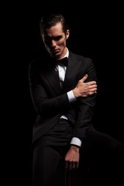 businessman pose seated in dark studio touching his arm 