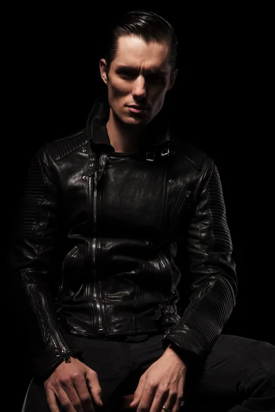 Sexy biker in black leather jacket posing seated in dark — ストック写真