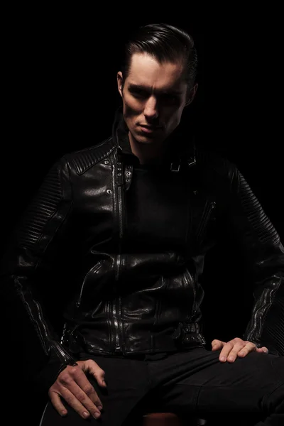 Man in black leather jacket posing seated in dark studio — Φωτογραφία Αρχείου