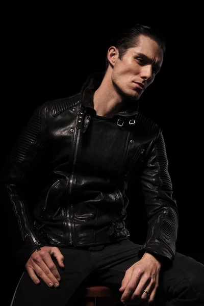 Roqueiro em jaqueta de couro posando sentado no escuro estúdio backgroun — Fotografia de Stock