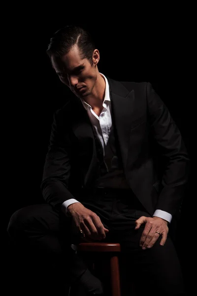 Young businessman in black suit seated in dark studio — Stok fotoğraf