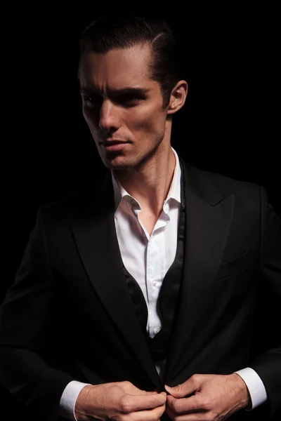 Businessman in black suit in dark studio closing his jacket — Zdjęcie stockowe