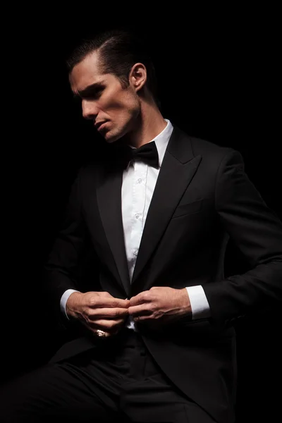 Businessman in black suit with bowtie posing seated in dark — Stok fotoğraf