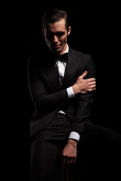 Attractive man in black pose seated touching his arm — Stock Photo, Image