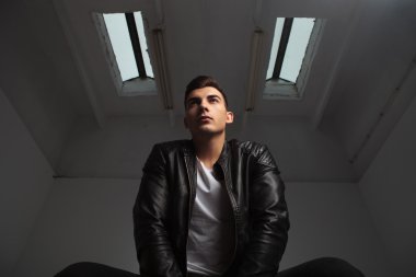 below view of young man in leather jacket posing seated