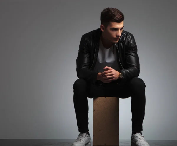 Young man in black leather jacket posing seated in studio — Stock Fotó