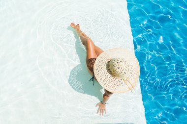 Yüzme havuzunda oturan beyaz şapkalı kadın