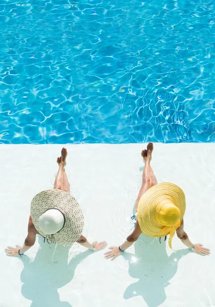 Dvě ženy v klobouku, sedí na okraji bazénu — Stock fotografie