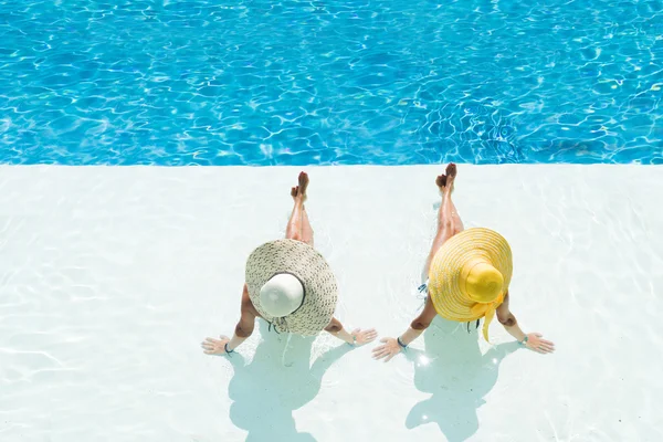 Dos mujeres en un sombrero sentadas en el borde de la piscina — Foto de Stock