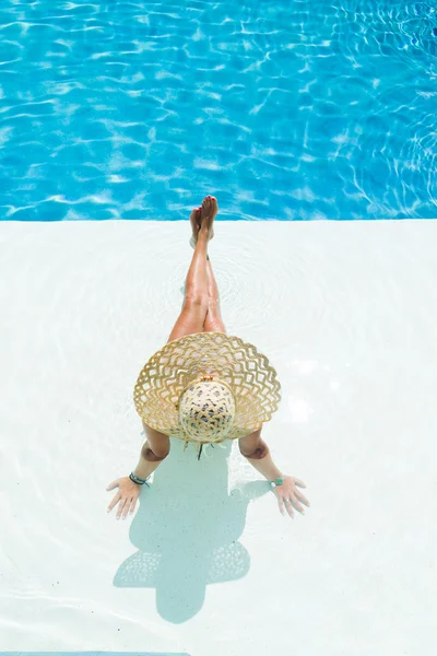 Mulher de chapéu branco sentada na piscina — Fotografia de Stock