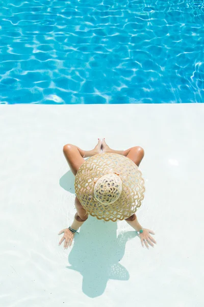 Vrouw in een witte hoed zitten bij het zwembad — Stockfoto