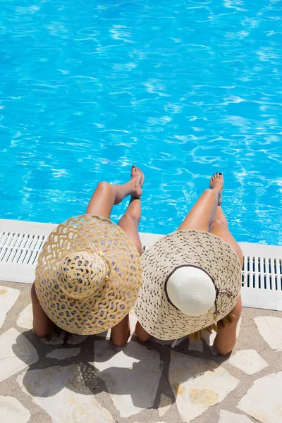 一顶帽子，坐在游泳池边上的两个女人 — 图库照片
