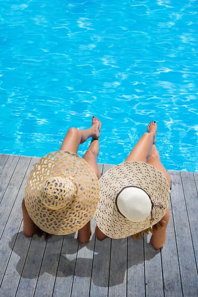 Duas mulheres de chapéu sentadas à beira da piscina — Fotografia de Stock