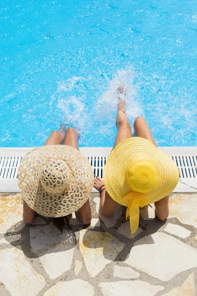 Two woman in a hat sitting on the edge of the pool — Stock Photo, Image