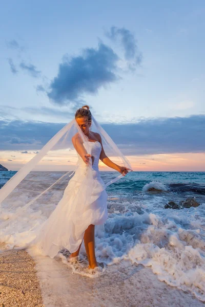 Bruid poseren tonen haar trouwjurk op het strand — Stockfoto