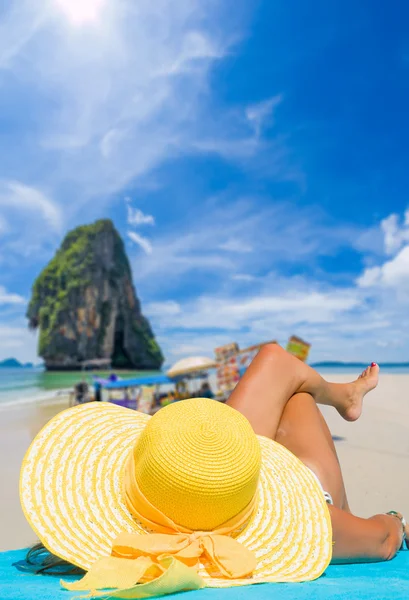 Młoda kobieta ubrana w bikini i niedz kapelusz, siedząc na plaży — Zdjęcie stockowe