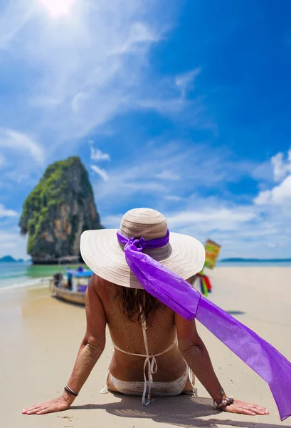 Jovem mulher vestindo um biquíni e chapéu de sol sentado na praia — Fotografia de Stock