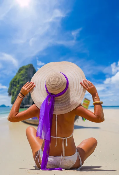 Giovane donna in bikini e cappello da sole seduta sulla spiaggia — Foto Stock