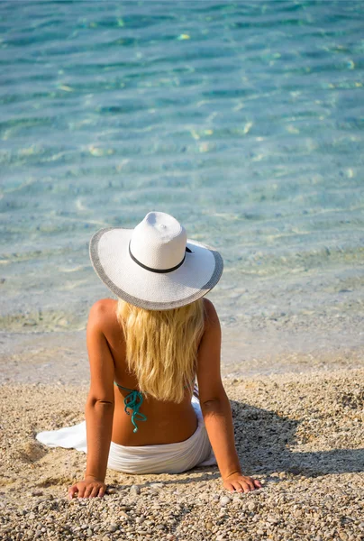 Prachtige blonde in bikini zittend op het strand — Stockfoto