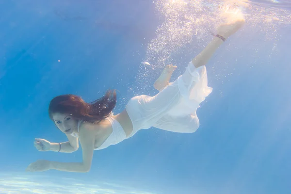 Mujer en un vestido blanco bajo el agua en la piscina — Foto de Stock