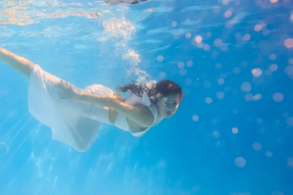 Mujer en un vestido blanco bajo el agua en la piscina — Foto de Stock