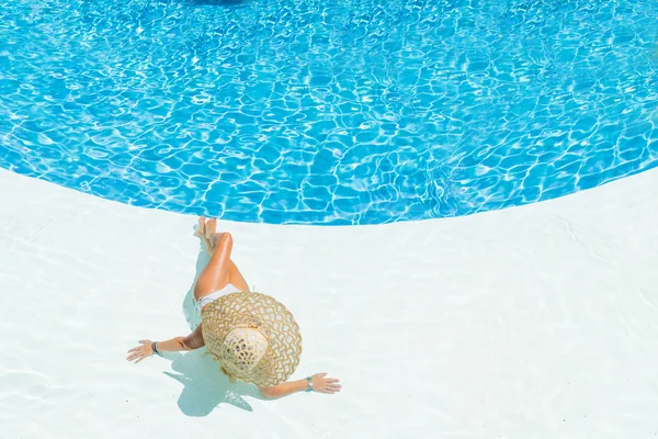 Beautiful woman in a hat sitting on the edge of the pool — Stock Photo, Image