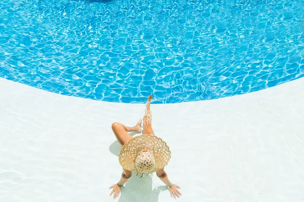 Bela mulher em um chapéu sentado na borda da piscina — Fotografia de Stock