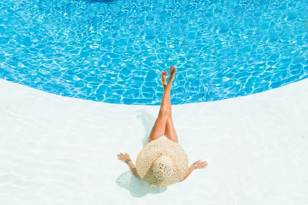 Beautiful woman in a hat sitting on the edge of the pool — Stock Photo, Image