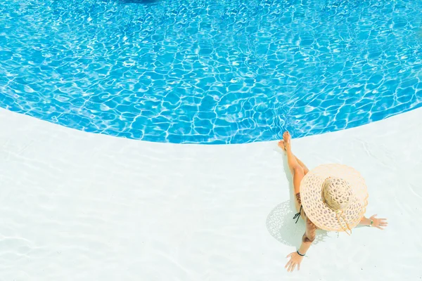 Schöne Frau mit Hut sitzt am Rande des Pools — Stockfoto