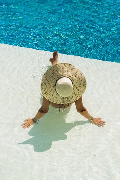 Bela mulher em um chapéu sentado na borda da piscina — Fotografia de Stock