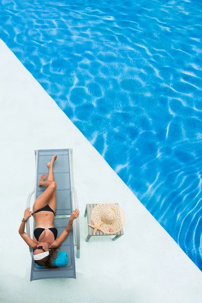 Bela mulher em um chapéu sentado na borda da piscina — Fotografia de Stock