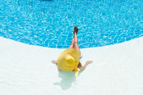 Schöne Frau mit Hut sitzt am Rande des Pools — Stockfoto