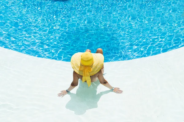 Mooie vrouw in een hoed zittend op de rand van het zwembad — Stockfoto