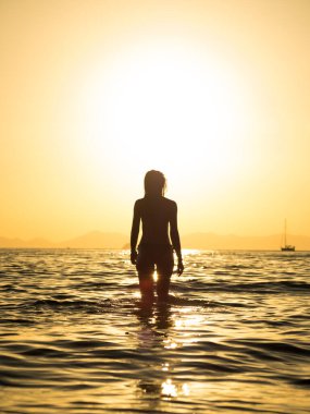 Gün batımında sahilde poz veren mayo giymiş bir kadın.