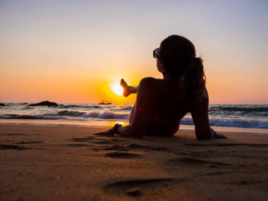 Gün batımında sahilde poz veren mayo giymiş bir kadın.