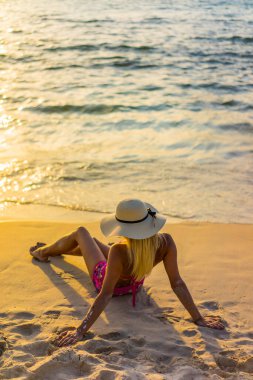 Gün batımında sahilde poz veren mayo giymiş bir kadın.