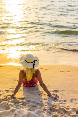 Gün batımında sahilde poz veren mayo giymiş bir kadın.