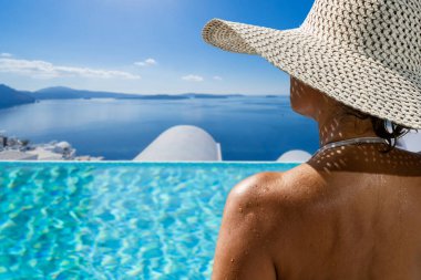 Yunanistan 'ın Santorini adasındaki yüzme havuzunda, Caldera manzaralı lüks bir tatil yapan bir kadın.