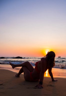 Gün batımında sahilde poz veren mayo giymiş bir kadın.