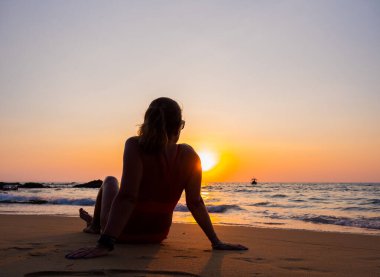 Gün batımında sahilde poz veren mayo giymiş bir kadın.