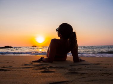 Gün batımında sahilde poz veren mayo giymiş bir kadın.