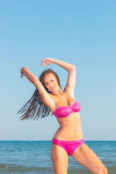 Mujer joven en bikini en la playa salpicando agua — Foto de Stock