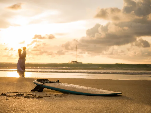 Prancha de surf e jovem casal ao pôr do sol em Bali islã — Fotografia de Stock