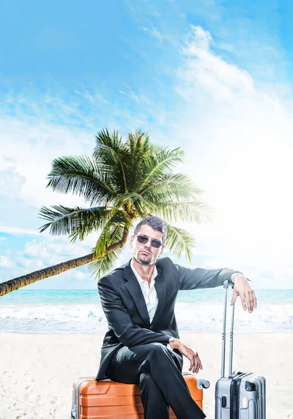 Man in suit sitting on a suitcase at the beach — Stock Photo, Image