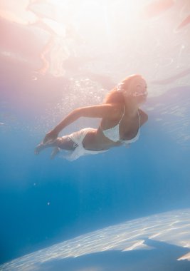 Genç bir kadın su altında yüzüyor.