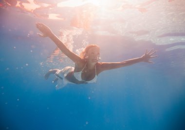 Genç bir kadın su altında yüzüyor.