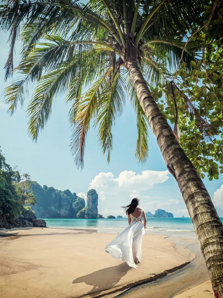 Woman in elegant wedding dress walking on beac — ストック写真