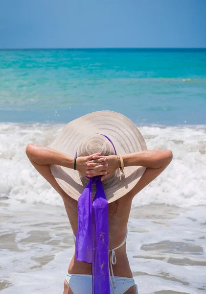 Back view of long haired young woman in swimsuit and straw hat o — Stock Photo, Image