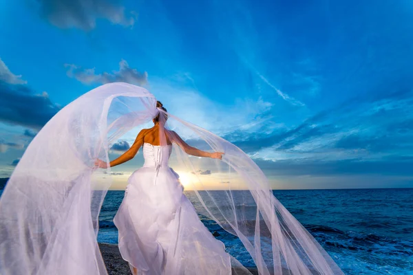 Jonge bruid door de zee bij zonsondergang — Stockfoto